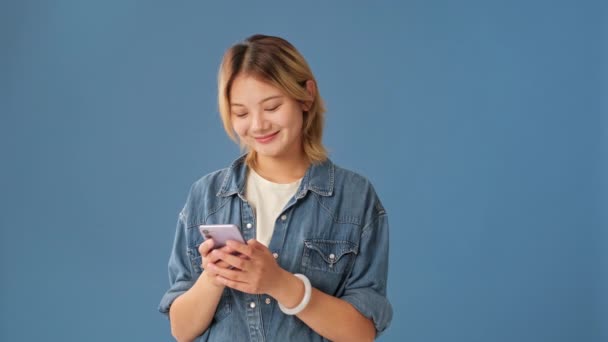Smějící Mladá Žena Baví Při Pohledu Mobilní Telefon Izolované Onblue — Stock video