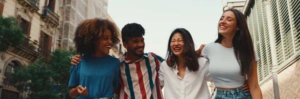 Mutlu çoklu etnik çeşitlilikte genç insanlar yaz günü açık havada kucaklaşarak yürürler, Panorama. Bir grup arkadaş sokakta yürürken neşeyle konuşuyor ve gülüyorlar.