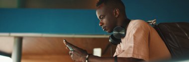 Kulaklıklı Afrikalı genç adam cep telefonu kullanıyor, Panorama.