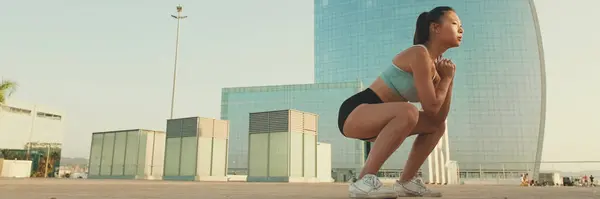 Asian girl in sports top does workout, squats, quadriceps exercises at morning time, Panorama