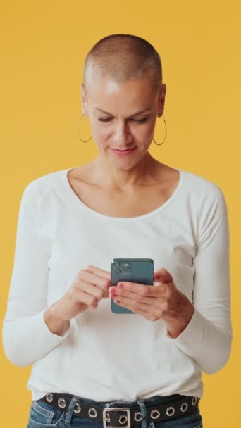 Uśmiechnięta Kobieta Przewijająca Telefon Komórkowy Odizolowana Żółtym Tle Studio — Wideo stockowe