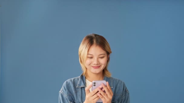 Sorrindo Jovem Mulher Usando Telefone Celular Isolado Fundo Azul — Vídeo de Stock