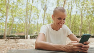 Parkta bankta otururken telefonda beyaz bluz tomarları giyen güzel bir kadın.