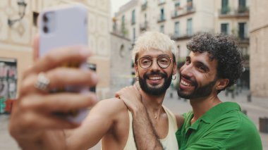 Eşcinsel çift ayağa kalkar ve cep telefonundan video görüşmesi yapar, selamlaşarak el sallarlar