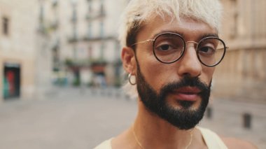 Sarı saçlı, gözlüklü, gülümseyen ve kameraya bakan yakışıklı bir adam.