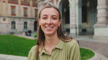 Eski şehrin arka planında kameraya bakan güzel, gülen bir kadının yakın çekimi.