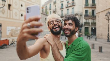 Eşcinsel çift ayağa kalkar ve cep telefonundan video görüşmesi yapar, selamlaşarak el sallarlar