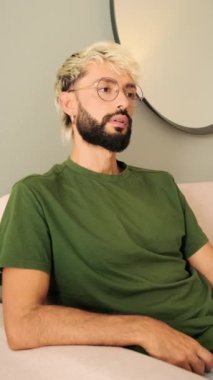 Sakallı genç sarışın adam rahat bir oturma odasında kanepede oturuyor.