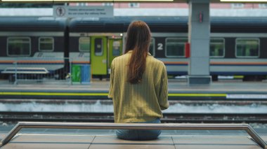 Bir tren istasyonunda bankta oturan genç bir kadın.
