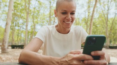 Beyaz bluz giyen güzel bir kadın bankta otururken telefon kullanıyor.