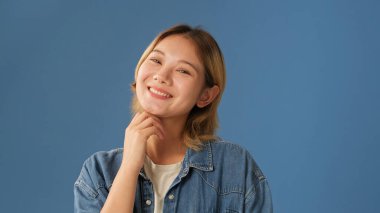 Stüdyoda mavi arka planda izole edilmiş kot gömlek giymiş, gülümseyen genç bir kadın.