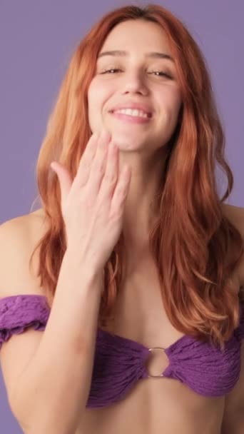 穿着紫色上衣的微笑的女孩在紫色背景上表现出了空中亲吻的姿态 — 图库视频影像