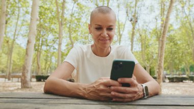 Beyaz bluz giyen güzel bir kadın bankta otururken telefon kullanıyor.