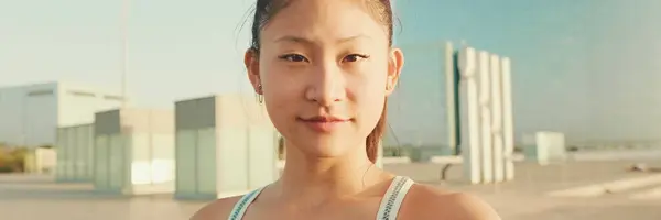 Smiling asian girl in sports top makes selfie while standing on the embankment in the morning light, look at camera, Panorama