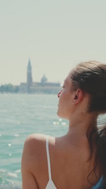 Dikey video, yakın çekim, uzun kahverengi saçlı, mavi gömlekli güzel kız, Venedik 'te sette oturuyor,