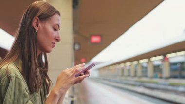 Bir tren istasyonundaki bankta otururken cep telefonu kullanan genç bir kadının yakın çekimi.