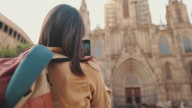 Kadın, eski bir Avrupa şehrinin tarihi bölümünde dururken cep telefonuyla fotoğraf çekiyor.