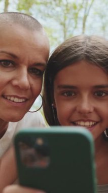 Kapatın, mutlu anne ve kız parkta cep telefonuyla oturuyorlar.