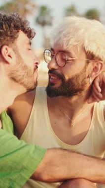 Homoseksüel çift sahilde otururken sarılıp öpüşüyor.