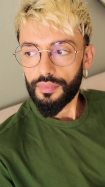 Yakın plan, sakallı genç sarışın adam rahat bir oturma odasında koltukta oturuyor.