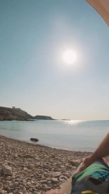 Pov çekimi, adam güneşlenir, etrafa bakar, ayağa kalkar ve suya girer.