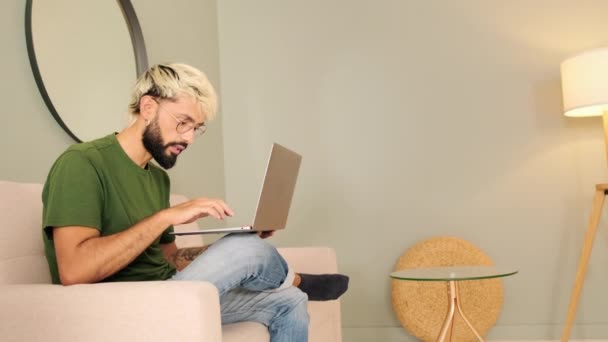 坐在舒适的客厅里 一个留着胡子的金发年轻人在笔记本电脑上工作 — 图库视频影像