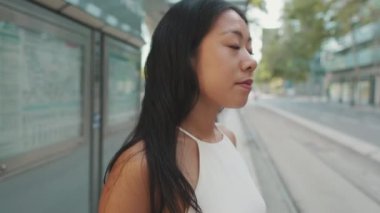 Toplu taşıma durağında durup etrafa bakınan genç bir kadının yakın çekimi.