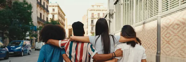 Mutlu çoklu etnik çeşitlilikte genç insanlar yaz günü açık havada, arka planda, Panorama 'da kucaklaşarak yürürler. Bir grup arkadaş sokakta yürürken neşeyle konuşuyor ve gülüyorlar.