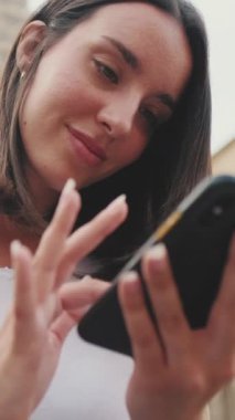 Kadın gezgin, arka plandaki eski bir binanın merdivenlerinde otururken cep telefonu kullanıyor.