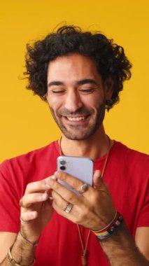 Akıllı telefondan iyi haberler okuyan adam, sarı arka planda izole edilmiş stüdyoda zaferi kutluyor.