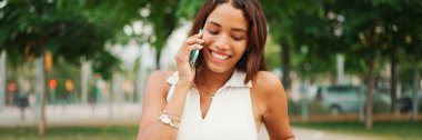 Uzun siyah saçlı, beyaz bluzlu güzel bir kız parktaki bankta oturuyor ve Panorama 'da cep telefonu kullanıyor. Cep telefonuyla konuşan genç bir kadın.