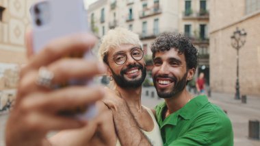 Eşcinsel çift ayağa kalkar ve cep telefonundan video görüşmesi yapar, selamlaşarak el sallarlar