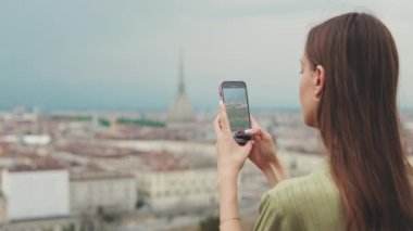 Şehrin gözlem güvertesindeki genç kadın cep telefonuyla fotoğraf ve video çekiyor.