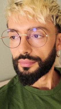 Yakın plan, sakallı genç sarışın adam rahat bir oturma odasında koltukta oturur ve yan tarafa bakar.