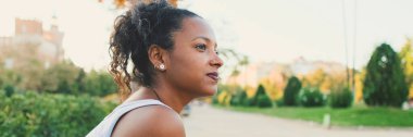 Genç melez kadın parkta oturuyor, gülümsüyor, etrafa bakıyor, Panorama