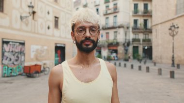 Sarı saçlı, gözlüklü, gülümseyen ve kameraya bakan yakışıklı bir adam.