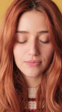 Yakın plan, gözlerini açan kız sarı arka plandaki kameraya bakıyor.