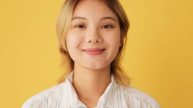 Yakın plan, kadın gözlerini açar ve kameraya bakar. Stüdyoda sarı arka planda izole edilmiş bir gülümseme ile.