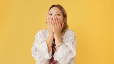 Gömlek ve kravat takmış, sarı arka planda izole edilmiş mutluluğu ifade eden şaşırmış genç bir kadın.