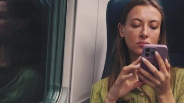 Trenle seyahat ederken cep telefonu kullanan genç bir kadın.