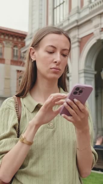 かわいい女性は古い町の広場に立っている間彼女の携帯電話の地図アプリを使用します — ストック動画