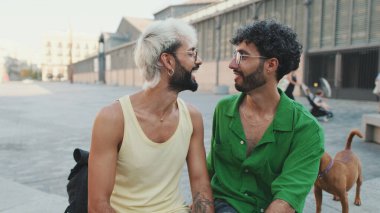 İki erkek turist sokakta otururken sohbet ediyorlar.