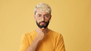 Gözlüklü, sarı tişörtlü adam, dikkatle dinliyor ve kabul ediyor, stüdyoda sarı arka planda izole edilmiş.