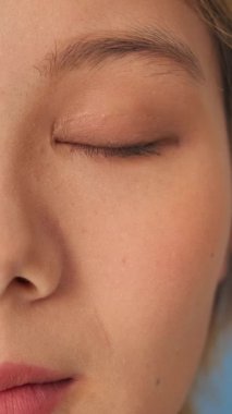 Portre kadını gözlerini açar ve mavi arka plandaki stüdyoda izole edilmiş kameraya bakar.