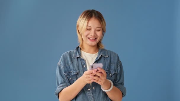 Skrattar Ung Kvinna Som Har Roligt Tittar Mobiltelefon Isolerad Blå — Stockvideo