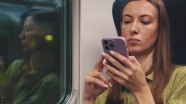 Akıllı telefonlu genç bir kadın trenle seyahat ediyor.