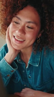 Oturma odasında dizüstü bilgisayarla konuşan gülümseyen genç bir kadın.