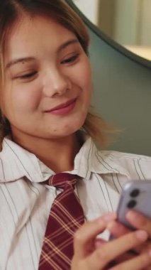 Oturma odasındaki koltukta oturan akıllı telefon cihazıyla gülümseyen kadın.