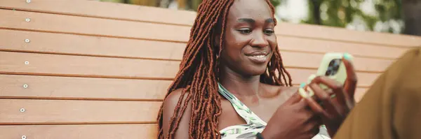Uśmiechnięta Piękna Kobieta Afrykańskimi Warkoczami Górze Używa Telefonu Komórkowego Siedząc — Zdjęcie stockowe