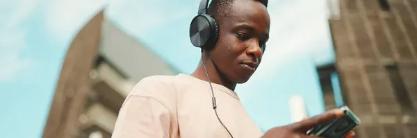 Joven Estudiante Africano Sentado Fuera Universidad Usando Auriculares Usando Teléfono — Foto de Stock
